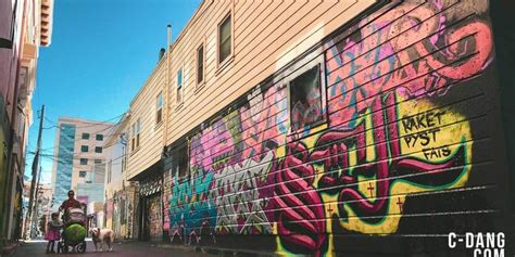 People Walking Down An Alleyway With Graffiti On The Wall And Buildings