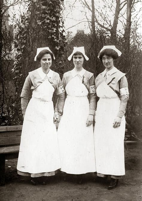 Three Women In Aprons And Hats Standing Next To Each Other Near A Park Bench