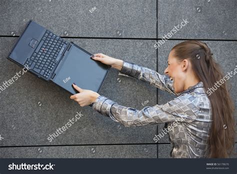Angry Woman Smashing A Laptop Computer Against The Wall Stock Photo