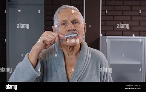 attractive old senior man grandfather in bathrobe brushing teeth looking into mirror handsome