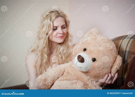 Young Blond Sensual Woman Sitting On Sofa Relaxing With A Huge Teddy