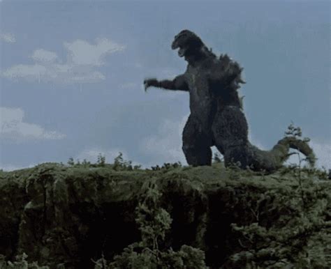 A Large Godzilla Standing On Top Of A Lush Green Hillside
