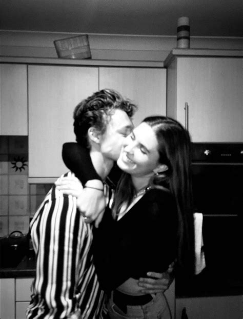 A Man Kissing A Woman In The Kitchen With His Arm Around Her Neck And She S Wearing A Striped Shirt