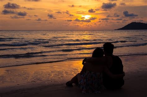 Pareja Joven Sentada En La Playa Con Puesta De Sol Foto Premium