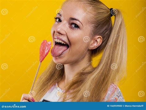 Beautiful Blond Girl Sticks Out Her Tongue To Taste A Pink Lollipop