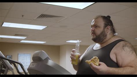 Obese Man Eating A Slice Of Pizza While Walking On The Treadmill In Gym