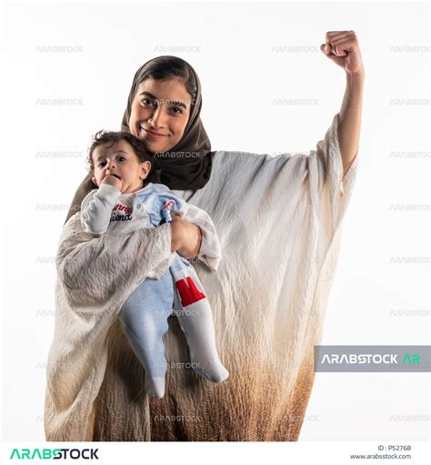 بورتريه لأم عربية خليجية سعودية، تحمل طفلها الرضيع بحب وحنان، ترفع يدها لأعلى بإيماءات تدل على