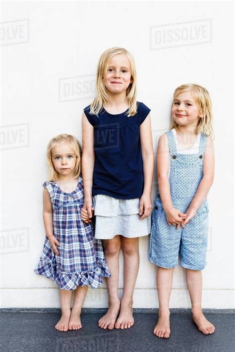 Portrait Of Three Young Sisters Standing In Front Of White Wall Stock
