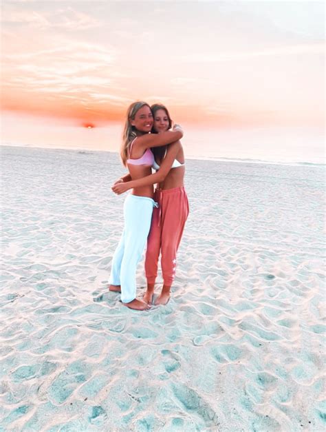 Two Women Hugging Each Other On The Beach In Front Of An Orange And