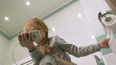 Little Girl Sitting On The Potty Into The Toilet With A Smartphone In