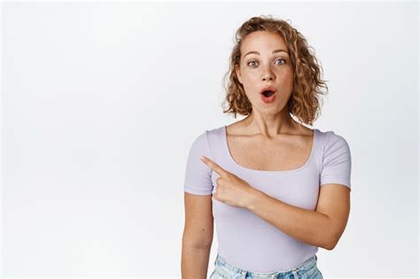 Free Photo Portrait Of Blond Curly Girl Looking Surprised Pointing Finger Left With Intrigued