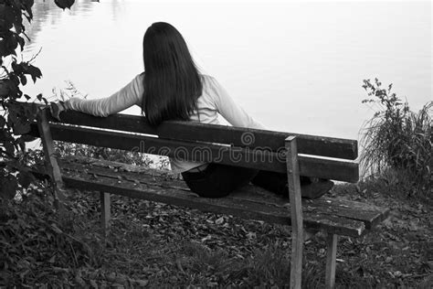 A Beautiful Young Girl Sitting On The Bench Looking Sadly At The Lake