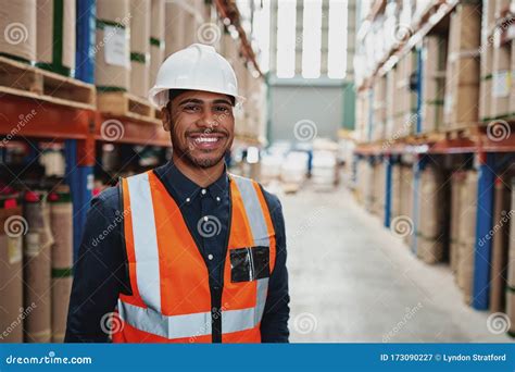 Happy Male Supervisor In Warehouse Standing In Uniform With White