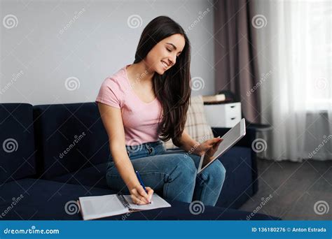 Cheerful Young Woman Sit On Sofa In Room And Look On Tablet She Write In Notebook Model Smiles