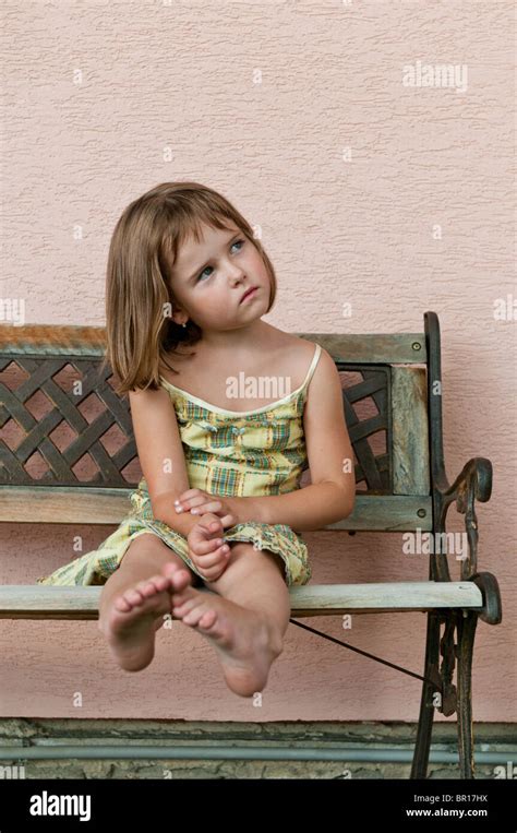 Portrait Of Cute Child Sitting On Bench And Stretching Barefoot Legs