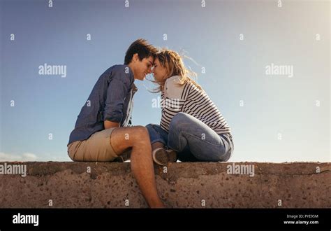 Romantic Couple Sitting Opposite To Each Other On A Sea Wall Touching