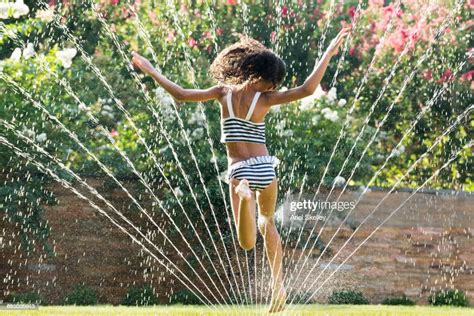 Mixed Race Girl Jumping In Backyard Sprinkler Photo Getty Images