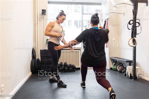 Personal Trainer Assisting A Woman Doing Exercises In Gym Female