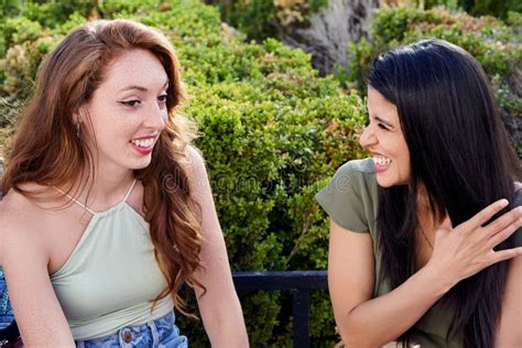 Two Female Friends Talking And Laughing While Sitting On A Bench In A