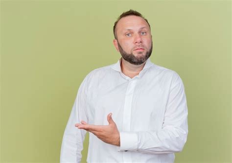 Homme Barbu Portant Une Chemise Blanche à Mécontent Avec Les Bras à La Hanche Debout Sur Un Mur