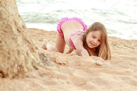 Красивая улыбка маленькая девочка в розовый купальник играет в песке на
