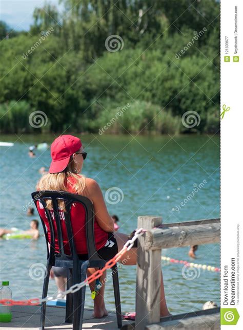 lifeguard sitting on chair with umbrella in front of the lake on back view editorial image