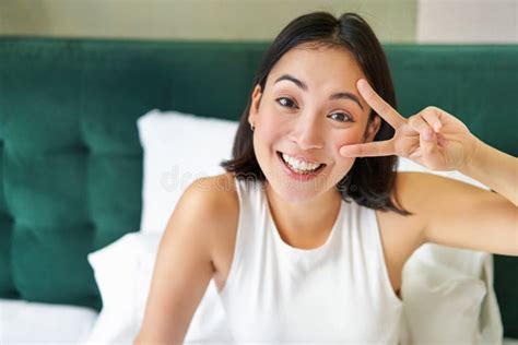 Positive Asian Woman Lying In Bed Showing Peace Sign Enjoys Happy