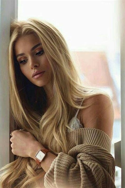 A Woman With Long Blonde Hair Leaning Against A Wall Wearing A Watch And Looking Off Into The