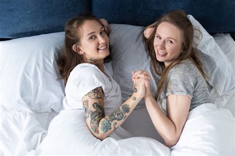 Two Laughing Lesbians Holding Hands While Lying On Bed In Morning