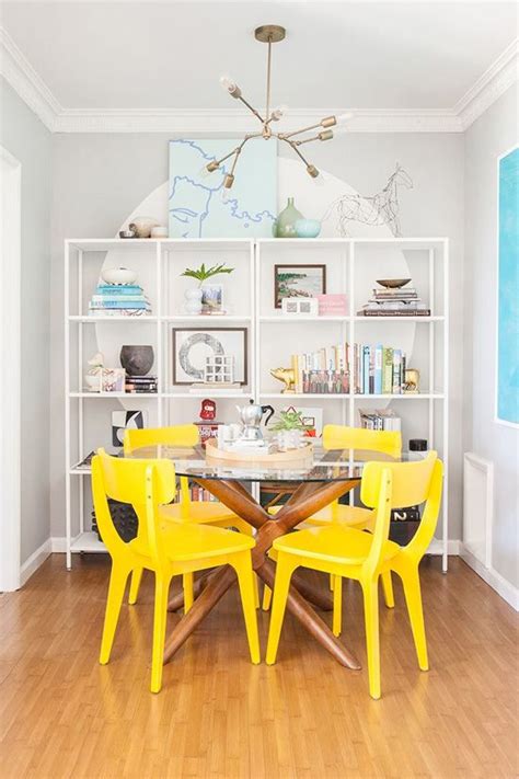 A Dining Room With Yellow Chairs And A White Bookcase In The Corner
