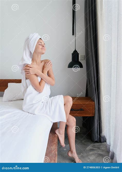 Woman Sitting On Bed After Shower With Wet Hair With Towel On Head In