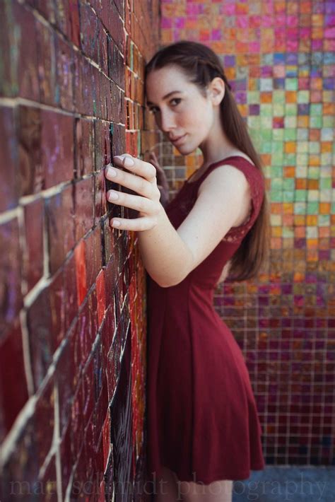 A Woman In A Red Dress Leaning Against A Brick Wall With Her Hand On
