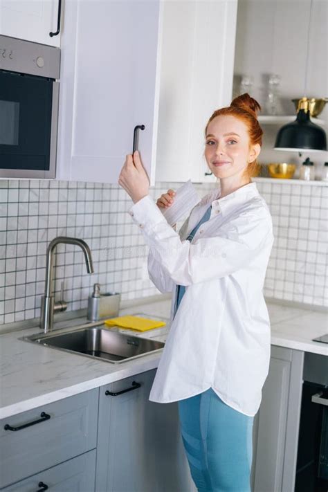 Side View Of Smiling Redhead Young Woman Opening Door Of Kitchen