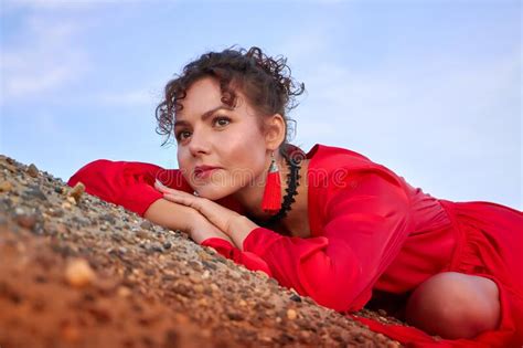 Portrait Of A Beautiful Young Woman Or Girl With Curly Hair And In A Red Dress On The Sand On