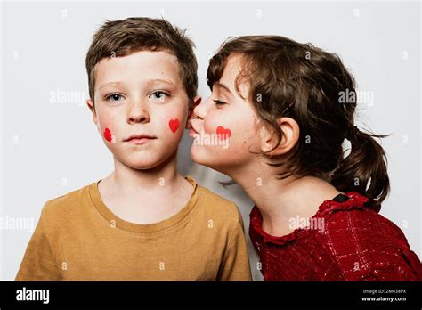 Cute Sister With Dark Hair Closing Eyes And Kissing Brother On Cheek Against Gray Background On