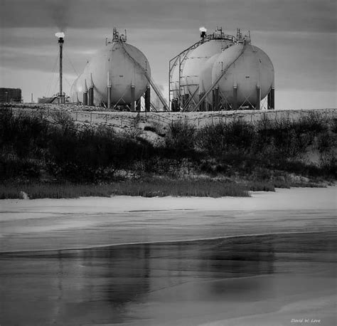 Black And White Photograph Of Two Large Tanks Near The Waters Edge On