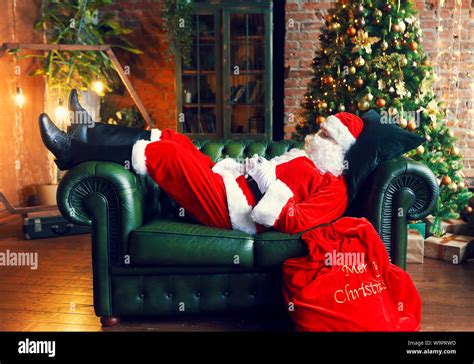 Santa Claus Sleeping At Home Near Christmas Tree On The Green Sofa