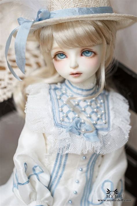 A Doll With Blonde Hair And Blue Eyes Wearing A White Dress Hat And Pearls