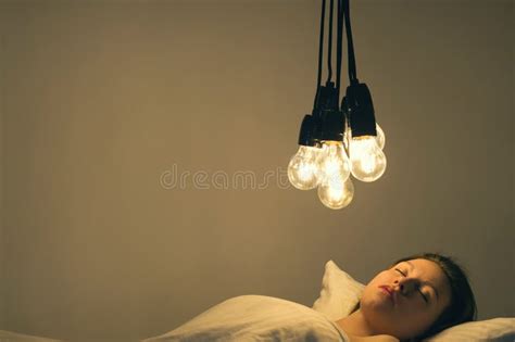 A Girl Lies In Bed Under Big Light Bulbs Can`t Fall Asleep Concept