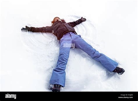 Young Cheerful Woman Lying Down On The White Clean Snow Making Snow