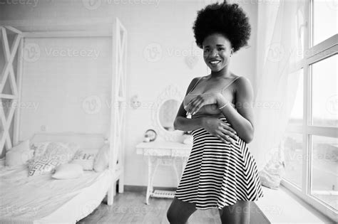 jolie femme afro américaine aux cheveux afro portant une jupe rose posée dans la salle blanche