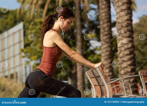 Young Sporty Woman Doing Stretching Workout By A Park Bench Outdoors