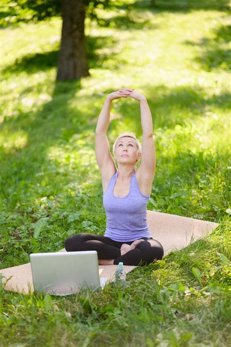 Athletic Middle Aged Woman Doing Online Yoga Outdoors In A City Park In