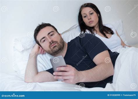 Man Neglecting His Girlfriend And Using His Mobile Phone In Bed Stock