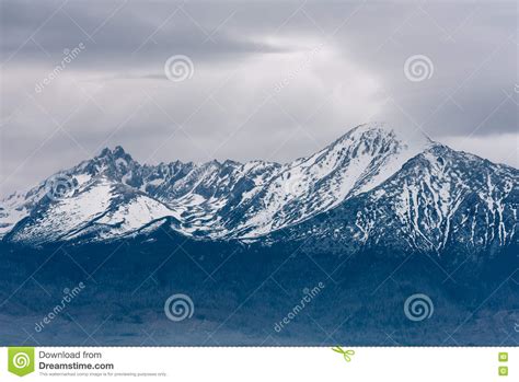 Snow Capped Peaks Of Rocky Mountains With Overcast Gray Sky Stock Photo