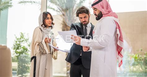 رجل اعمال عربي سعودي خليجي بالثوب السعودي التقليدي يتناقش مع عميل يرتدي البدلة الرسمية، اتفاقية