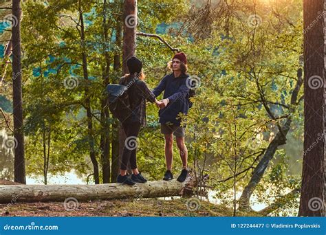 Young Hipster Couple Holding Hands Standing On A Tree Trunk In A