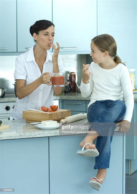Girl Sitting On Kitchen Counter While Mother Holds Up Container Of