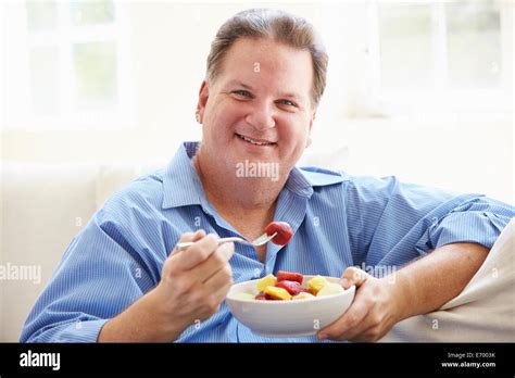Sobrepeso Hombre Sentado En El Sofá Comiendo Tazón De Fruta Fotografía