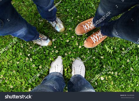 Group Of Friends Standing In A Circle On A Spring Meadow But Only Their Feet In Sneakers Is